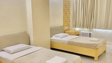 Une chambre d’hôtel avec deux lits simples, un canapé, un élément de séparation décoratif et une grande fenêtre avec des rideaux.