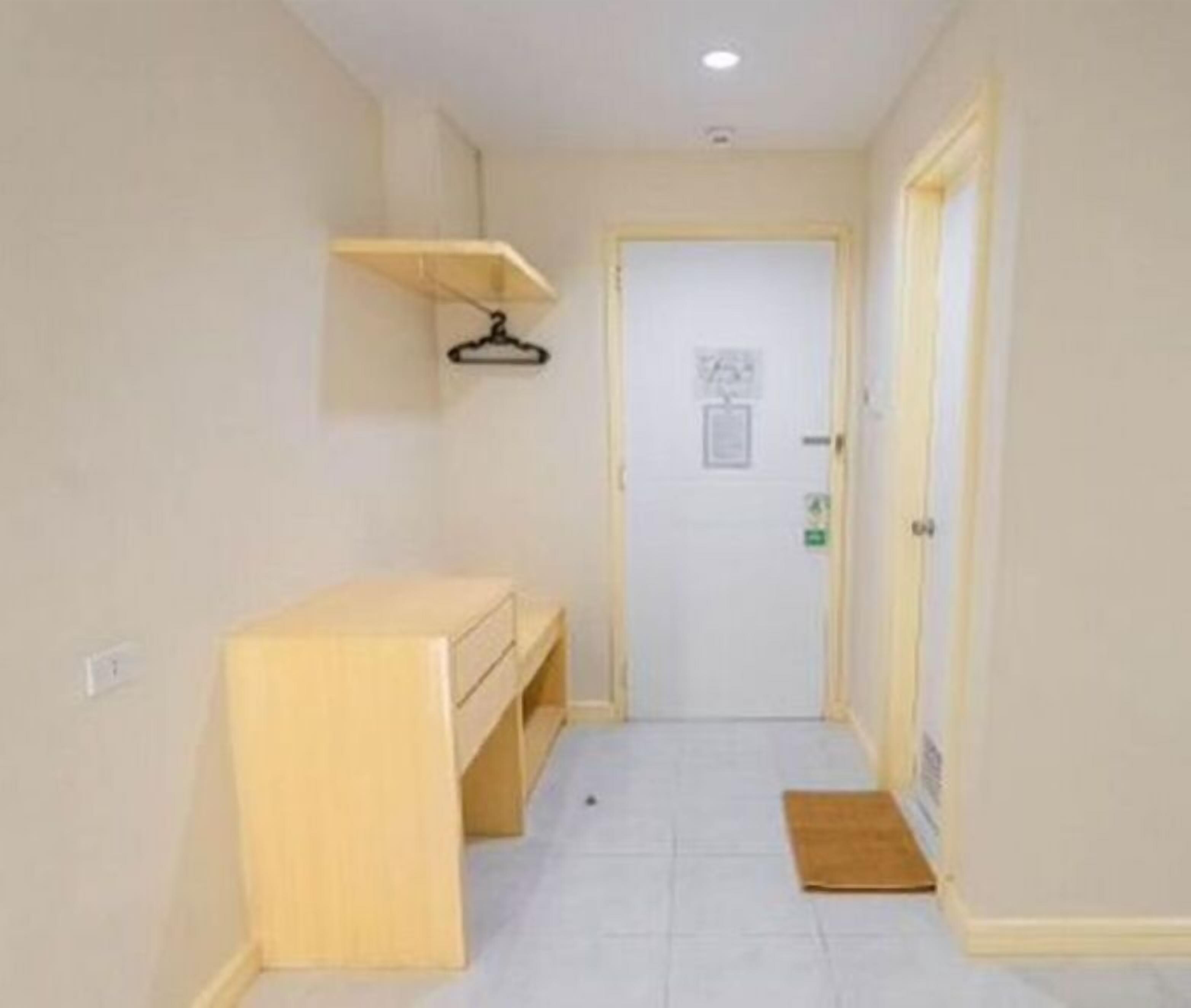 A narrow hallway with a wooden bench, a door at the end, and a small mat on the floor.