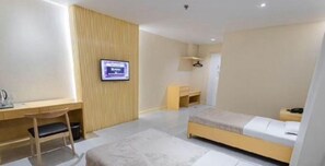 Una habitación de hotel moderna con un escritorio de madera, una cama, un televisor montado en la pared y un pequeño rincón de descanso.