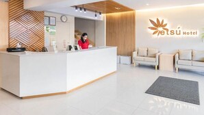 Ein Hotel-Empfangsbereich im modernen Stil, mit einer Rezeption, einer Rezeptionistin und einer Sitzecke mit zwei Sofas.