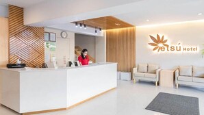 Zona de recepción de un hotel con diseño moderno, que incluye un mostrador, una recepcionista y un logotipo en la pared.