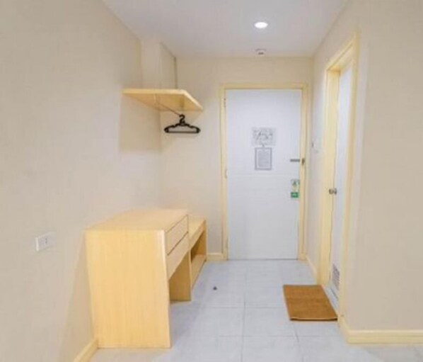 A narrow hallway with a wooden bench, a door at the end, and a small mat on the floor.