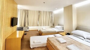 A hotel room with two beds, a wooden panel wall, a flat-screen TV, and a large window with curtains.