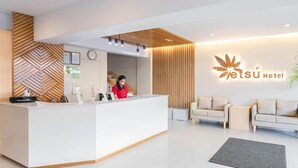 A hotel reception area with a modern design, featuring a reception desk, a clock, and a logo on the wall.