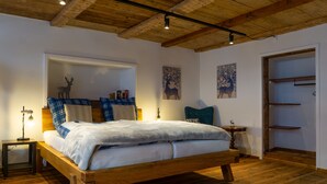 Un lit en bois avec une couette blanche, une table de chevet avec une lampe et un miroir orné d’une décoration représentant un cerf.