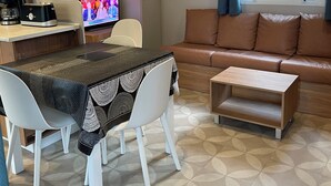 Een knus woongedeelte met een eethoek, een bank, een televisie en een raam met gordijnen.