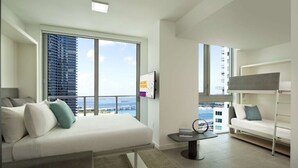 Un dormitorio moderno y bien iluminado con un ventanal grande, una cama, una mesita y un sofá.