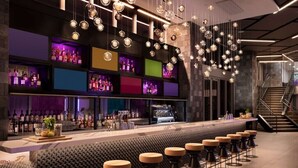 Zona de bar moderna con una barra larga, varios taburetes y lámparas esféricas colgantes.