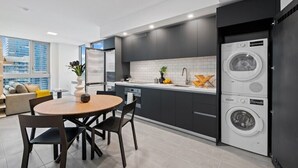 Une cuisine moderne avec des meubles de couleur sombre, un lave-linge encastré et un coin repas comprenant une table ronde et des chaises.