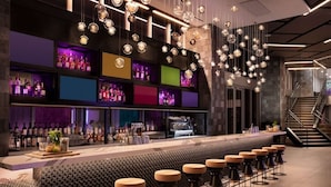 Un espace bar moderne doté d’un long comptoir, de nombreux tabourets et de luminaires sphériques suspendus.