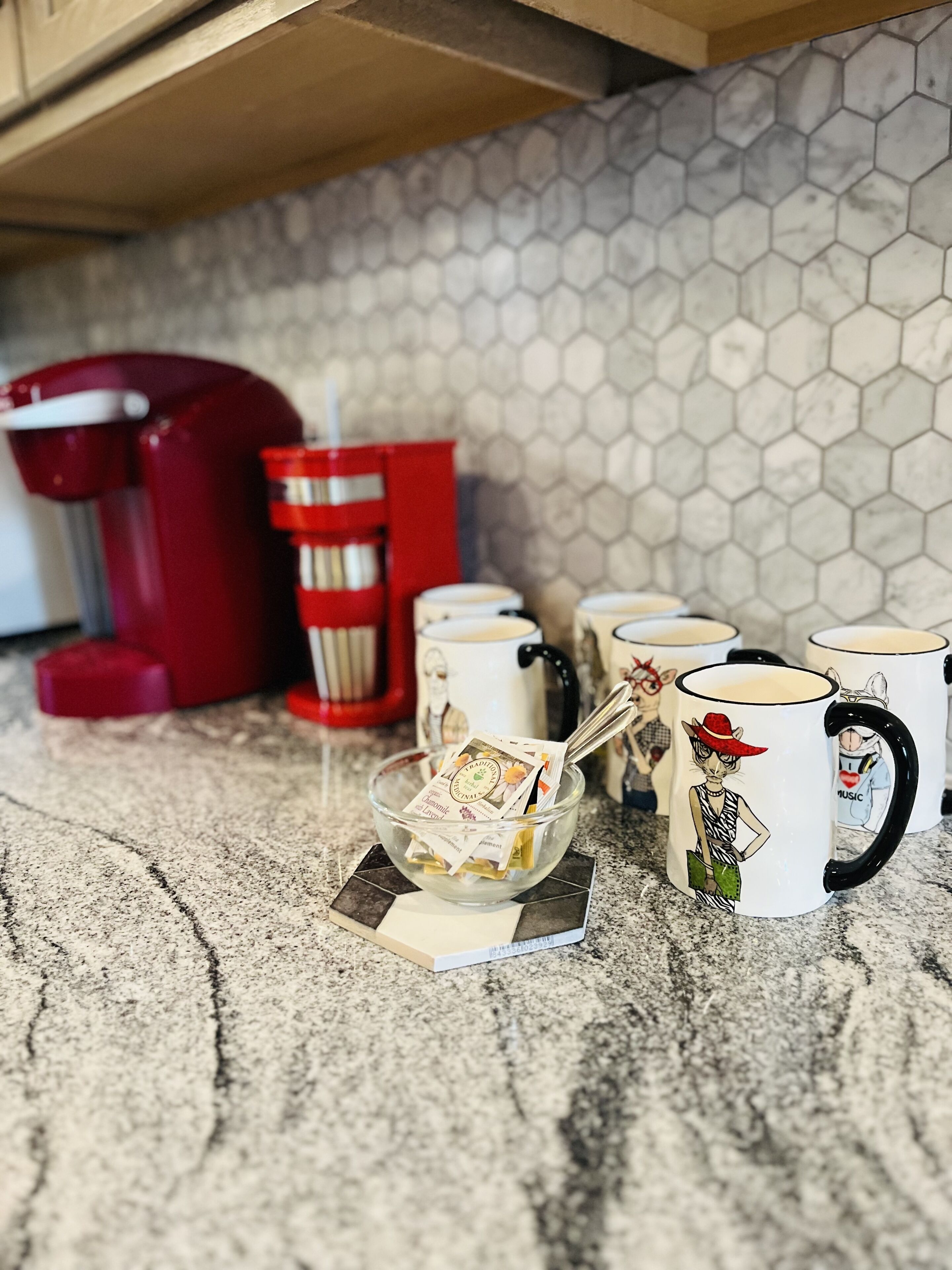 A kitchen counter with a coffee maker, a red appliance, and several mugs with cartoon characters.