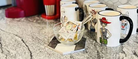 A kitchen counter with a coffee maker, a red appliance, and several mugs with cartoon characters.