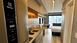 A modern hotel room with a kitchenette, a bed, a small seating area, and a view of the city. - Trends Brooklin (São Paulo)