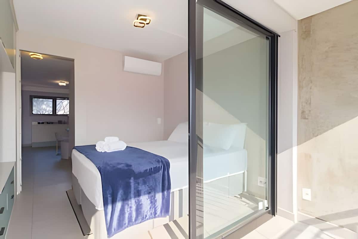 A modern hotel room with a bed, a desk, and a bathroom visible in the background.