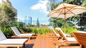 A wooden deck with lounge chairs and an umbrella, overlooking a cityscape. - Trends Brooklin (São Paulo)