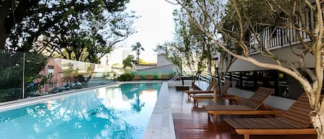 Una piscina al aire libre, sombrillas, sillones reclinables de piscina