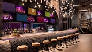 Un área de bar moderna con una barra alargada, varios taburetes y una gran variedad de botellas en estanterías.