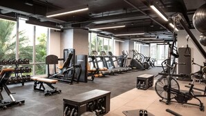 Un gimnasio con diverso equipo de ejercicios, amplias ventanas y vistas a palmeras.