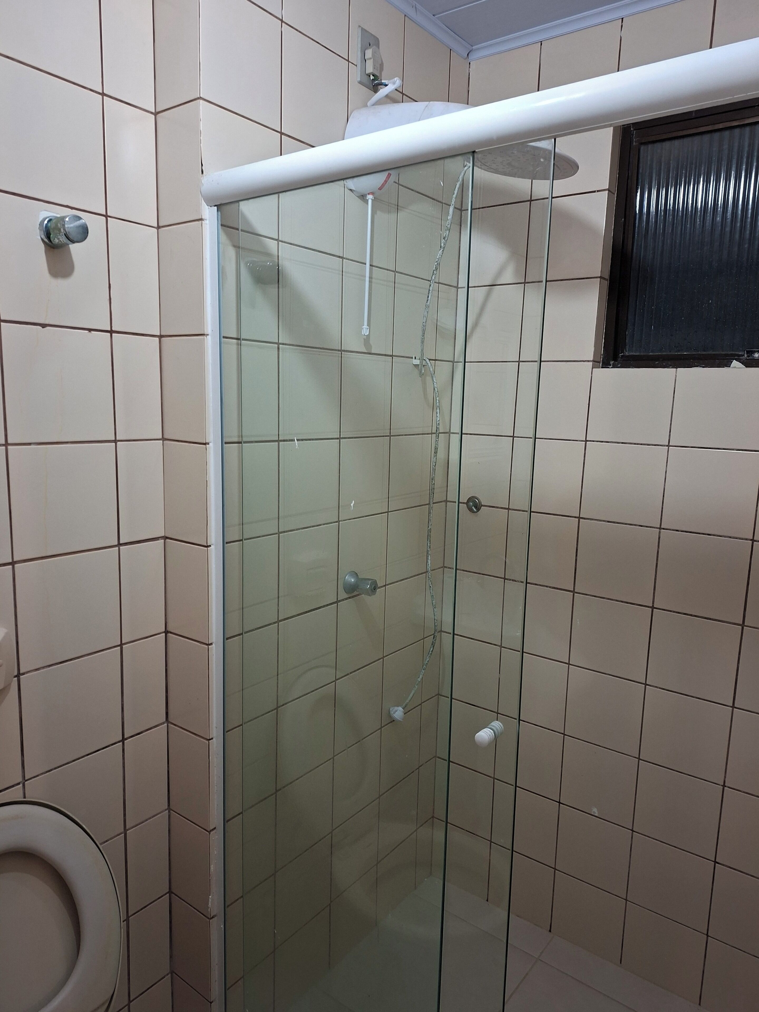 Box de chuveiro com paredes de azulejo, teto branco e vaso sanitário visível à esquerda.
