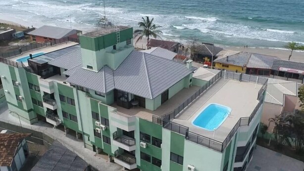 Un immeuble à plusieurs étages doté d’une piscine sur le toit, situé près d’une plage offrant une vue sur l’océan.