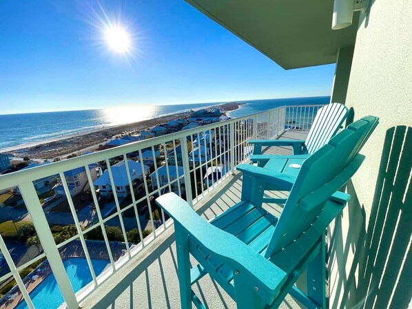 Un balcon avec des chaises turquoise donnant sur une plage et l’océan.
