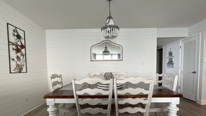 Un comedor con una mesa y sillas de madera, una araña y un espejo enmarcado sobre la mesa.