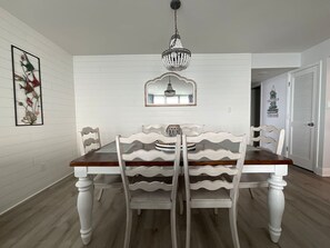 A dining area with a wooden table and chairs, a chandelier, and a framed mirror above the table. - Tristan Towers 13B • Corner Unit 2/2 • Best Views (Pensacola Beach)