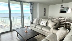 Una sala de estar moderna con un sofá gris, una mesa de centro de madera y vistas al mar a través de amplios ventanales.