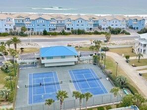 Zona residencial com duas quadras de tênis, um prédio com telhado azul e uma praia ao fundo.