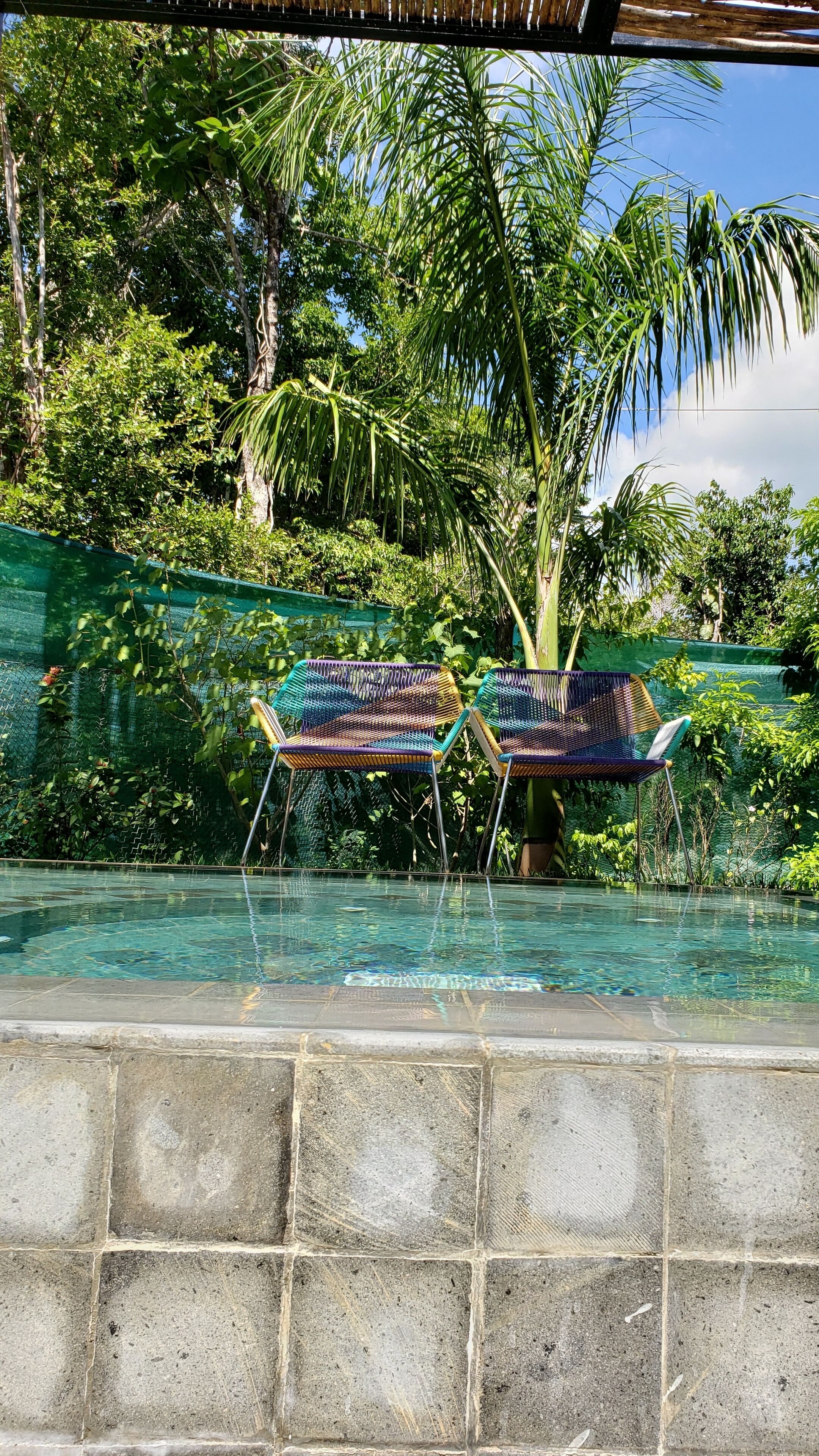 Zona de piscina con dos sillas coloridas y un muro de piedra.