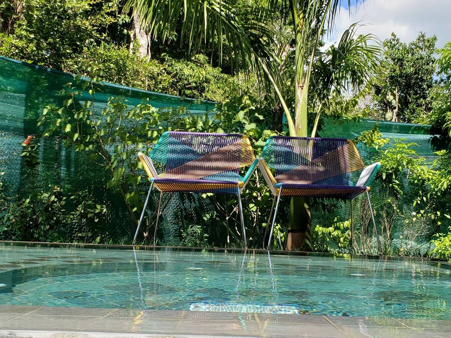 Zona de piscina con dos sillas coloridas y un muro de piedra.