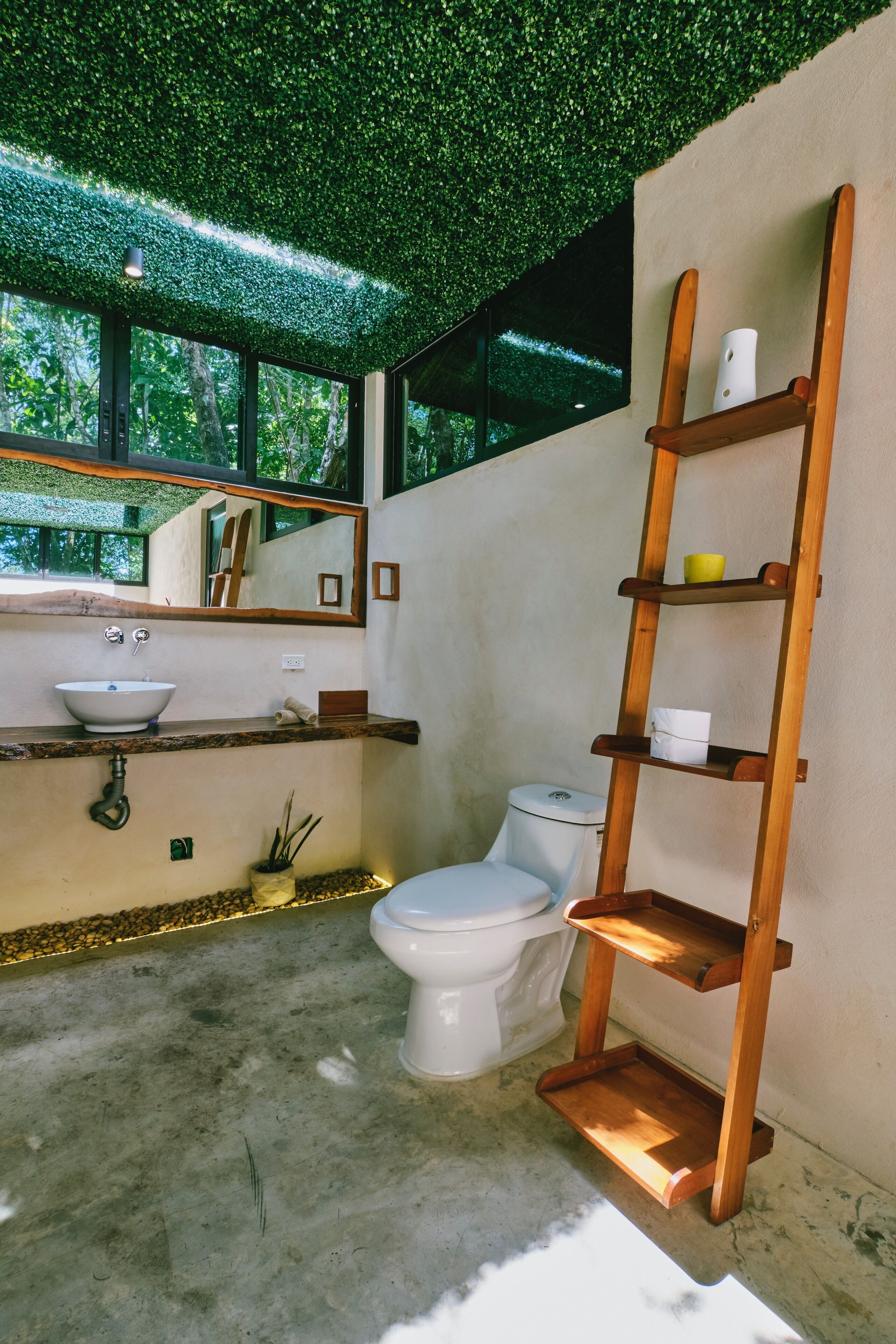 A bathroom with a green artificial ceiling, a white sink, a toilet, and a wooden shelf unit.