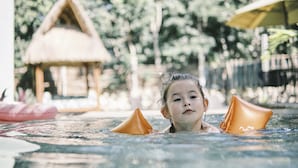 Una persona en una piscina con una cabaña de techo de paja al fondo.