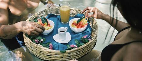 Una mesa de comedor con una cesta, tazones de comida y un vaso de jugo en un entorno junto a la piscina.