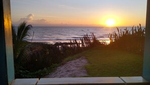 Uitzicht op de oceaan bij zonsondergang door een raam met houten kader en een betegelde vloer.