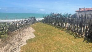 Uitzicht vanuit een overdekte ruimte op een strand, met een hek en een gebouw op de achtergrond.