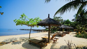 A beach with wooden lounge chairs and thatched umbrellas, a clear blue sky, and a calm sea. - Kiwuki Luxury Villa  (Phu Quoc)