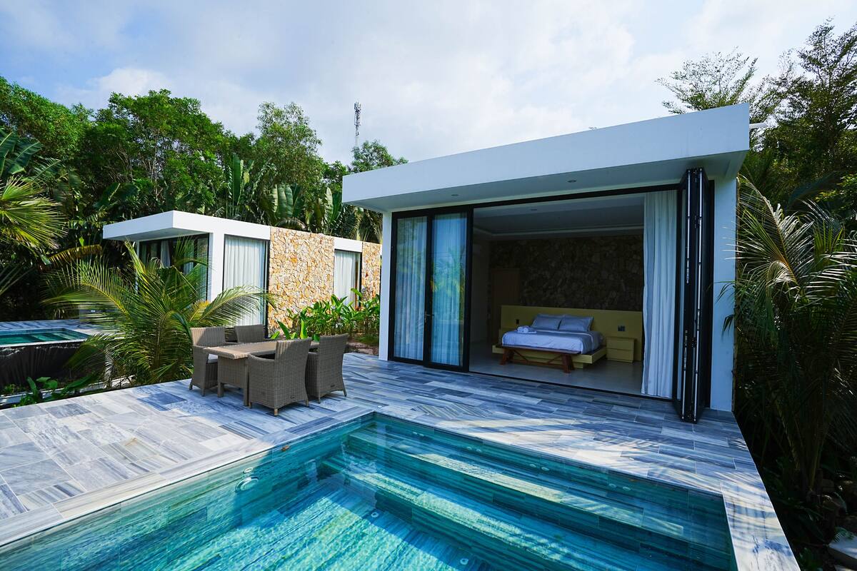 A modern villa with a swimming pool, a bedroom with a bed and a bathroom, and a dining area with outdoor furniture.