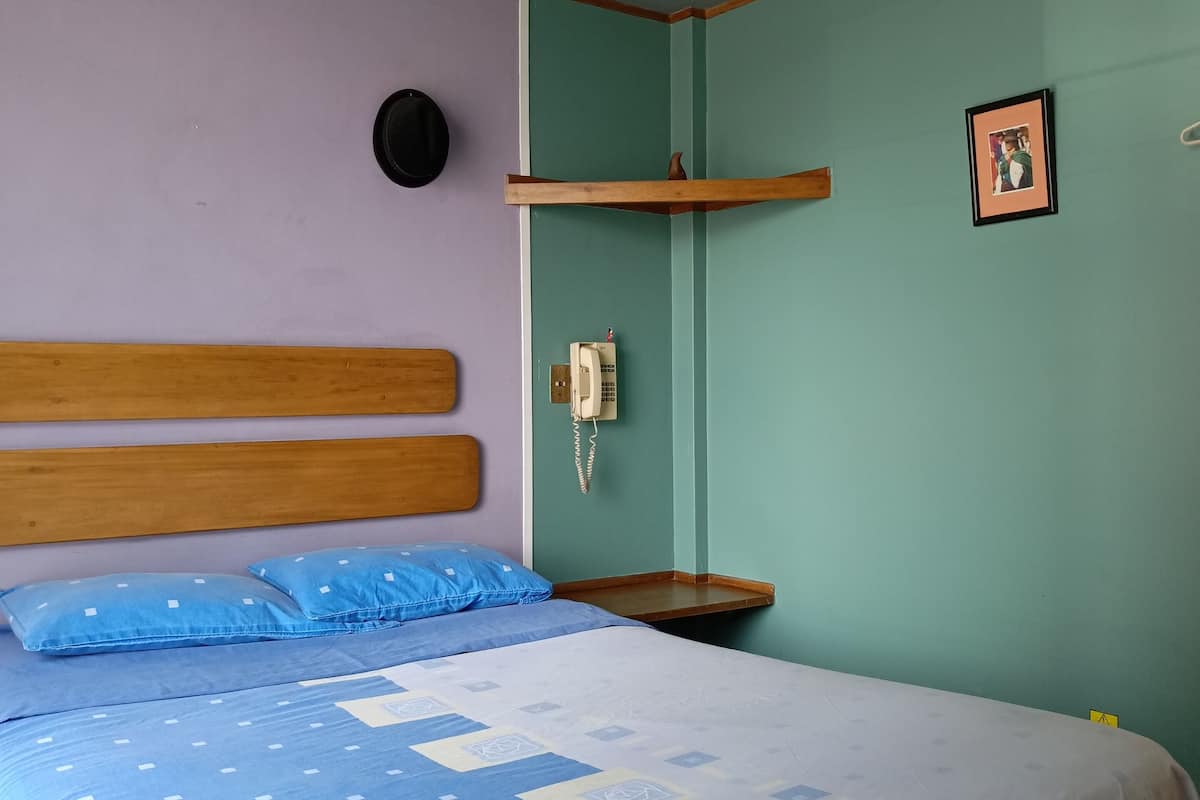 A bedroom with a bed, a wooden headboard, a wall-mounted phone, and a shelf.