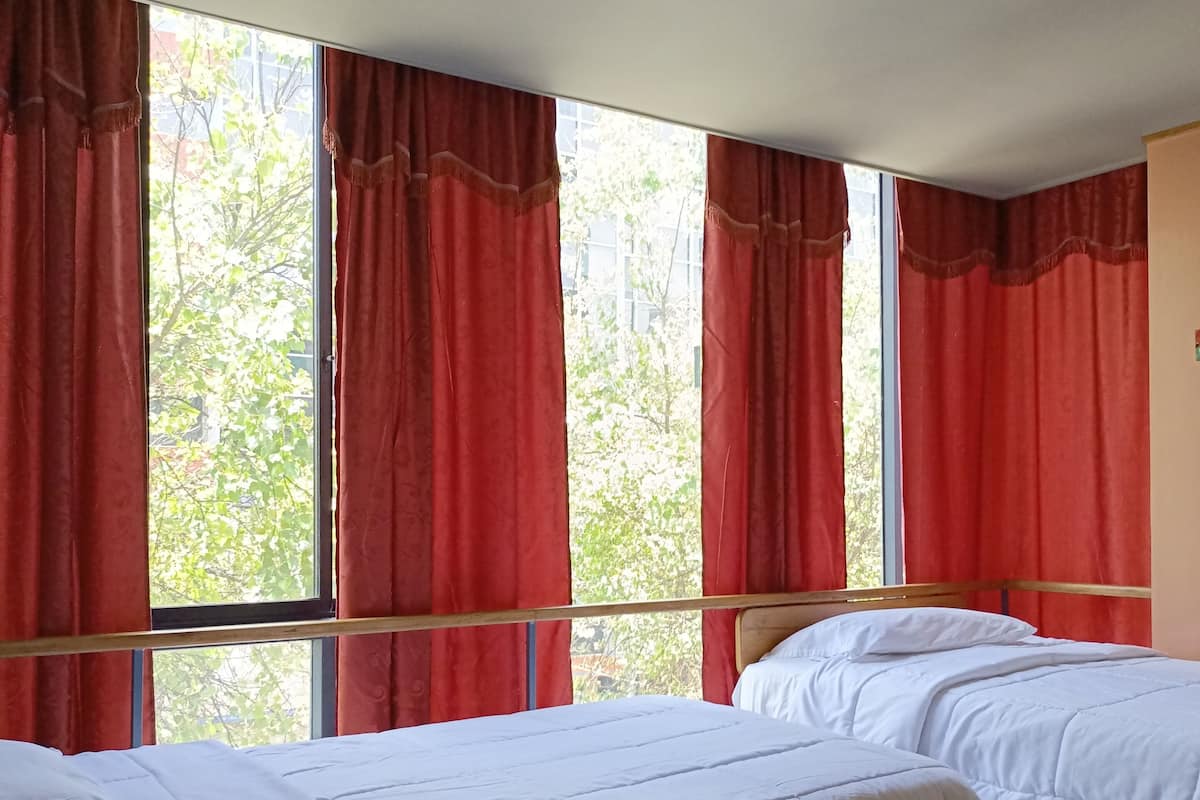 A room with two beds, red curtains, and a window with a view of trees.