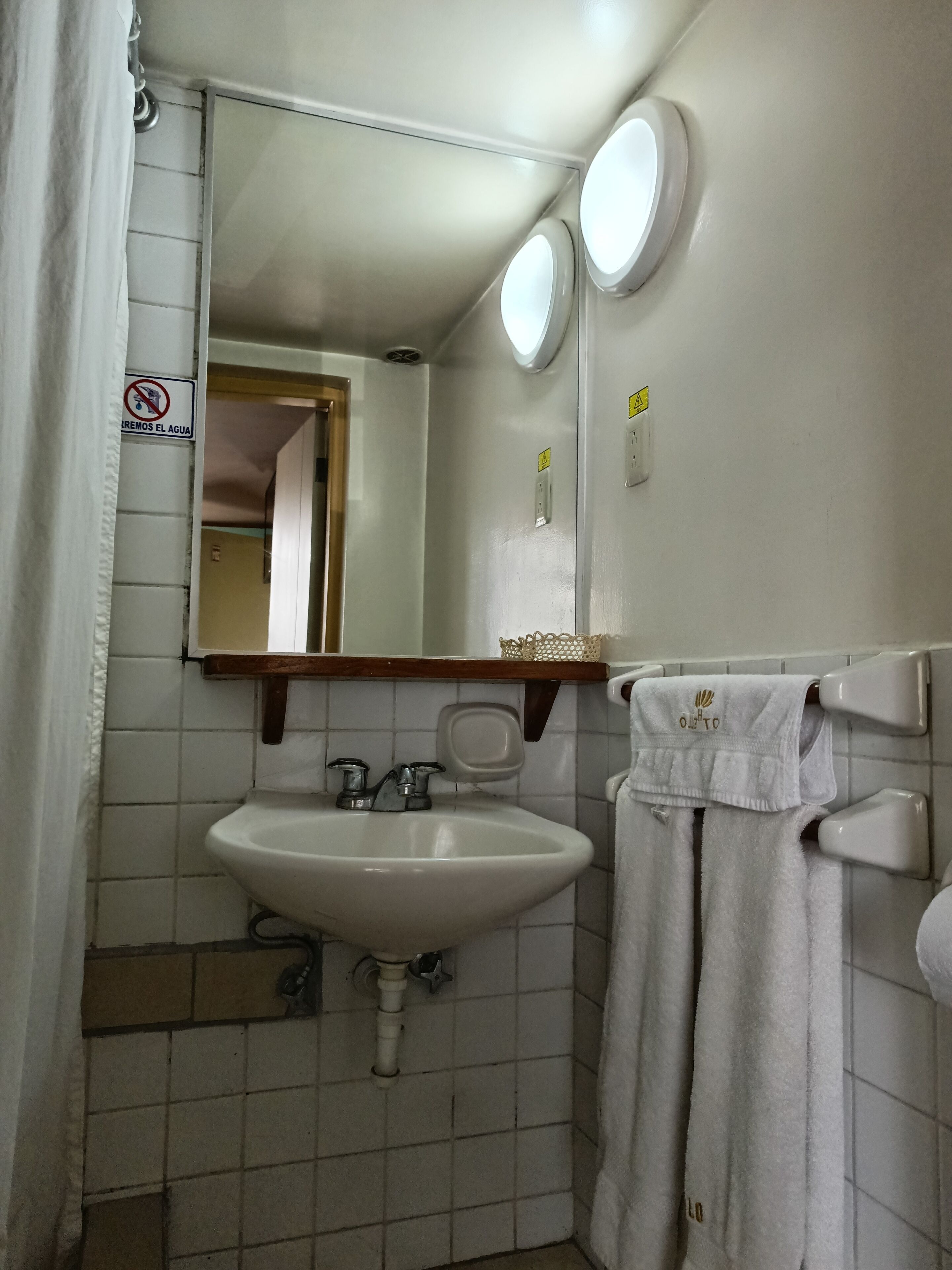 Un baño con lavamanos blanco, espejo y toallero.