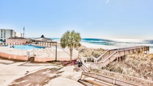 Zona de piscina con terraza de madera y una palmera, con vistas a la playa.