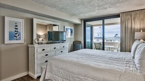 A hotel room with a large bed, a dresser, a TV, and a balcony with a view of buildings. - Beach Front, First Floor at Jetty East! One FREE Beach Chair Set Up Daily! (Destin)