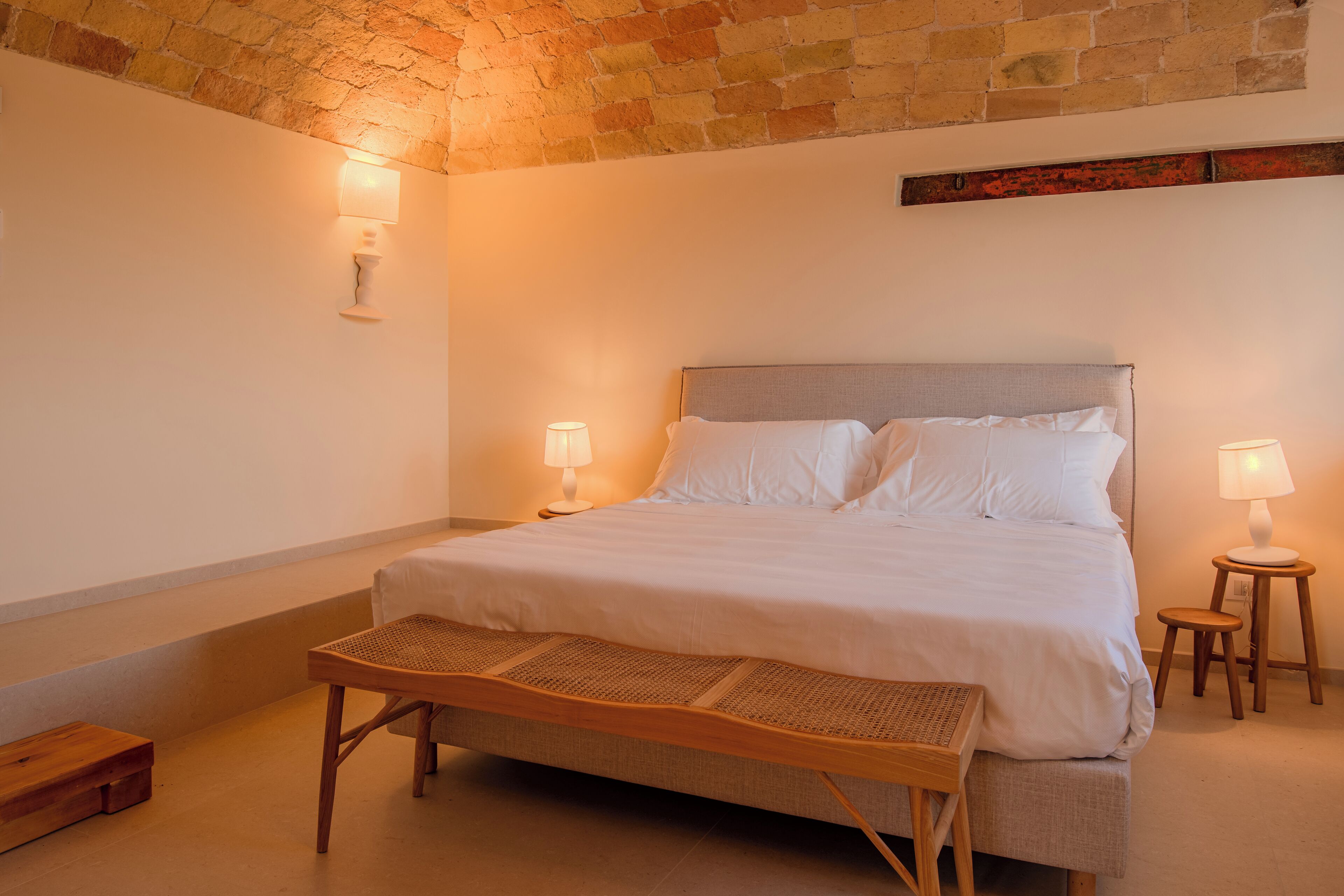 Ein Schlafzimmer mit einem Bett, zwei Nachttischen mit Lampen, einer Bank und einer Ziegelwand.
