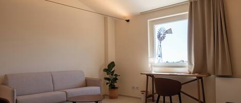 A living room with a sofa, a small table, a chair, a potted plant, and a window with curtains.
