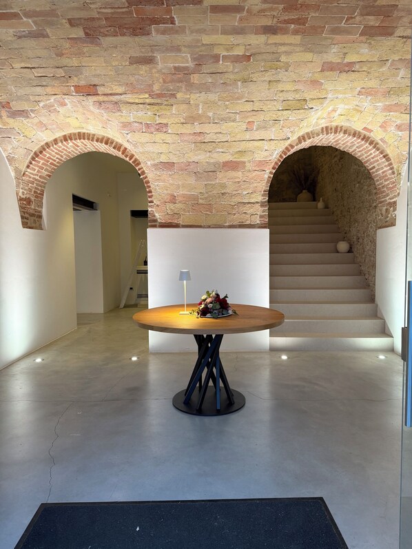 A modern interior with a round wooden table centered in a hallway, flanked by brick arches and a staircase. - Molikè Country House (Giulianova)