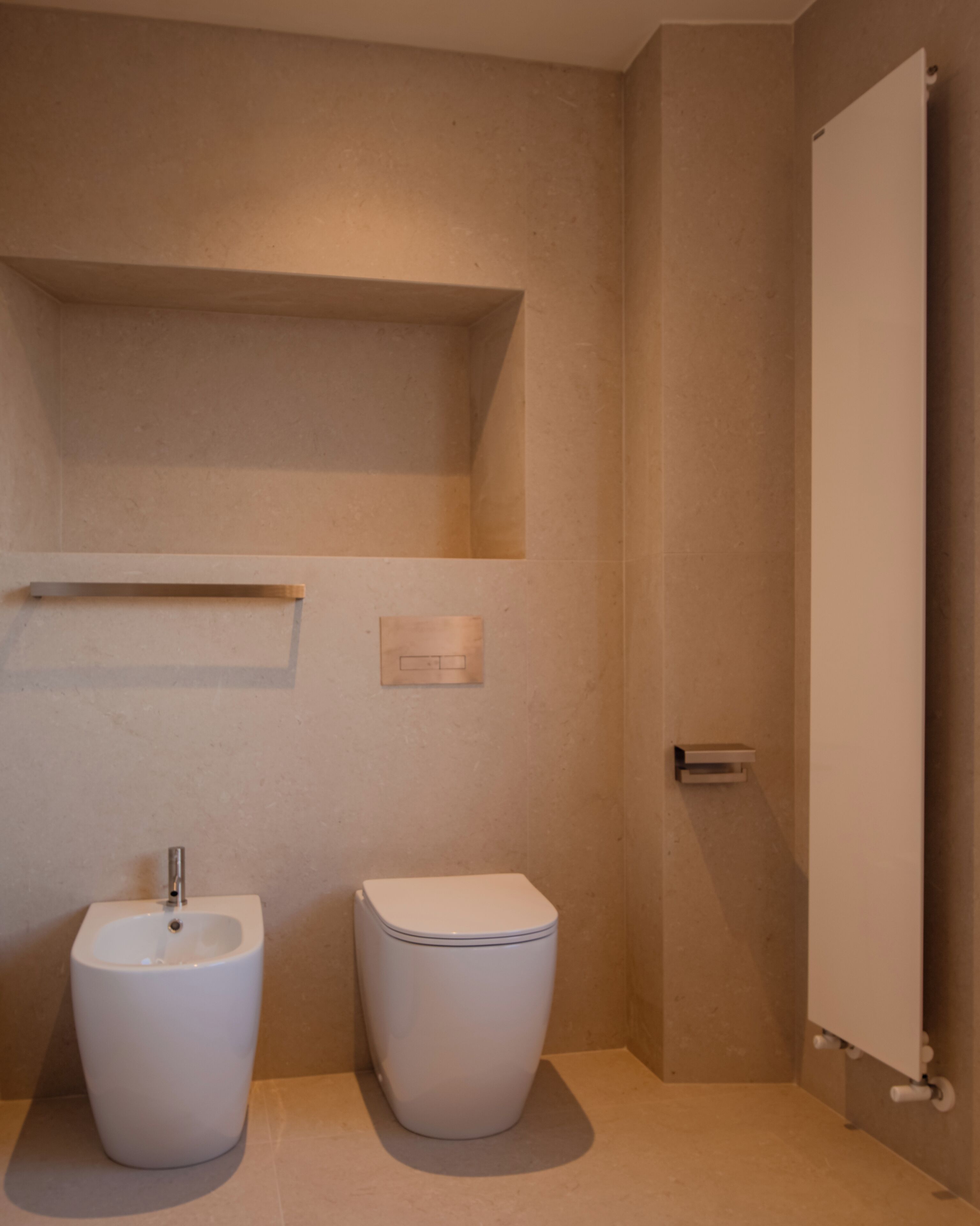 A modern bathroom with a bidet, a toilet, and a shelf above the toilet.
