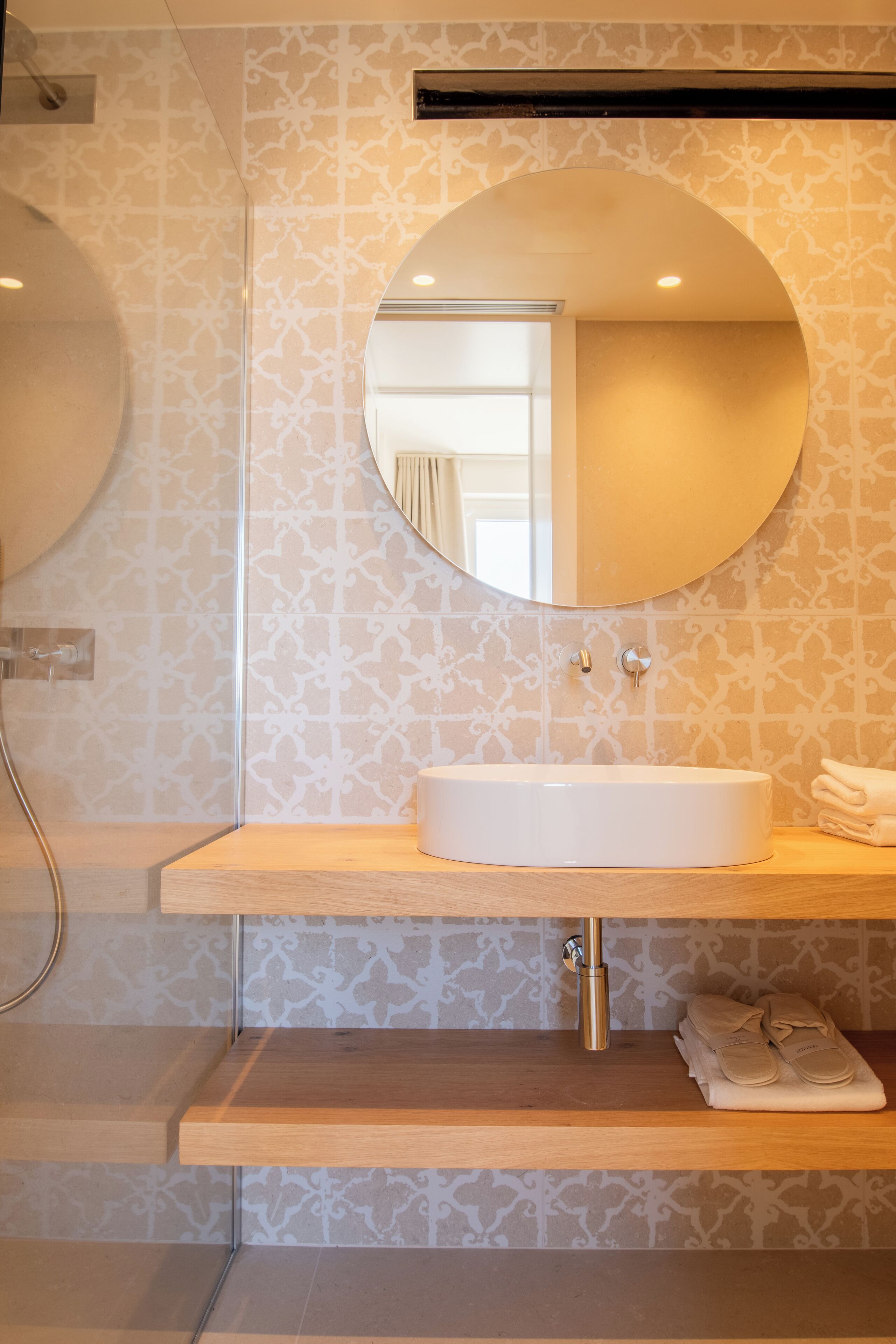A bathroom with a round mirror, a sink, and a towel rack.