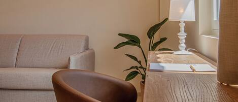 Un salon moderne avec un fauteuil en cuir marron, une table d’appoint en bois avec une lampe, un canapé beige et une plante en pot.