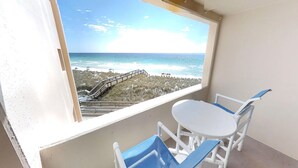 Ein Balkon mit Blick auf den Strand, ein weißer Stuhl und ein kleiner Tisch.